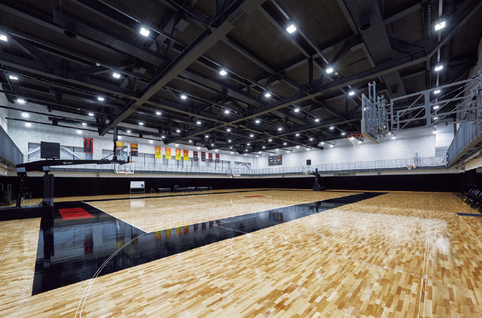 バスケットボールコート1面と、壁面にバスケットゴール4基が設置された練習場の高天井用照明器具と得点表示用LEDビジョン