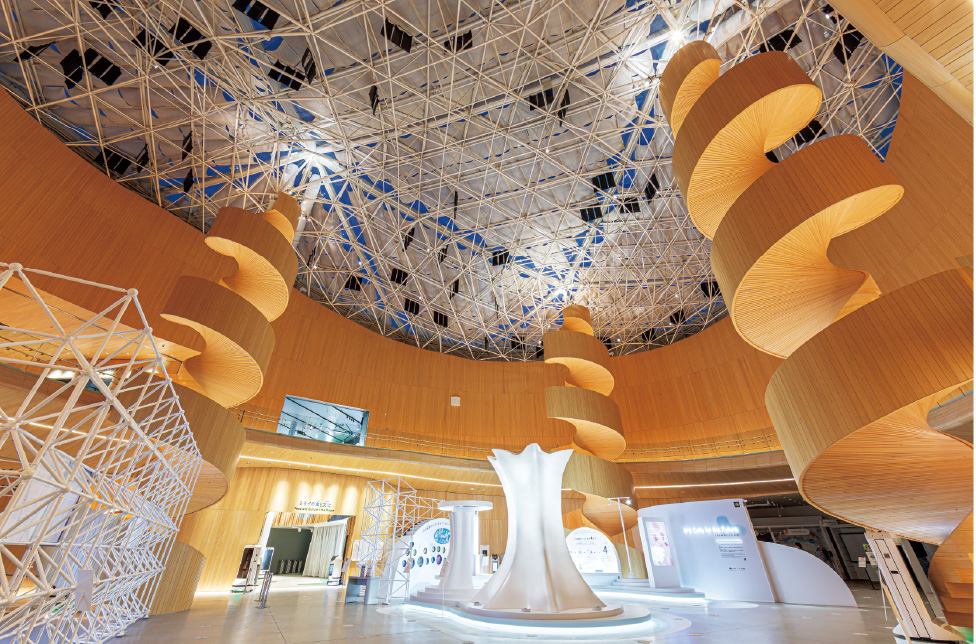 大阪府内産材で構成されたアトリウムには、DNAを模した螺旋状の柱が3本設けられている。螺旋状の柱と屋根を照射することにより、昼と夜で天井の明暗が反転する演出をしている