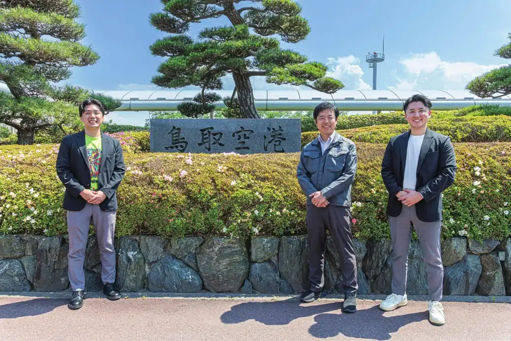 鳥取空港の看板前で撮影された熊田様・山陰パナソニック 土井様・当社山田の集合写真